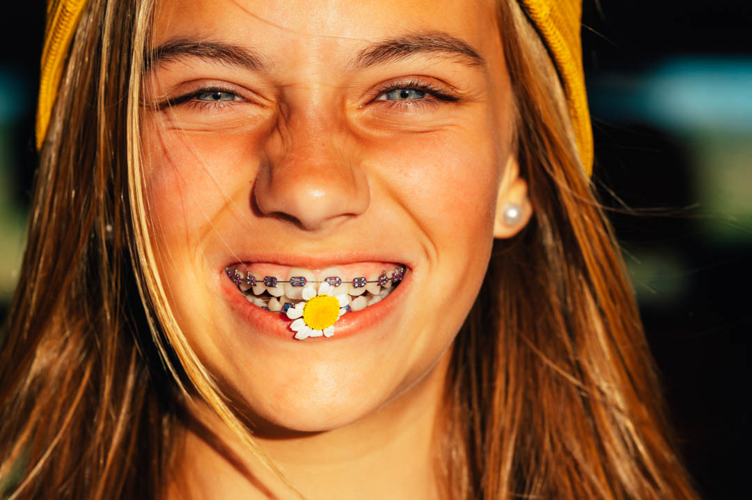Chica joven con brackets en los dientes sosteniendo una flor en la boca, mostrando una sonrisa radiante