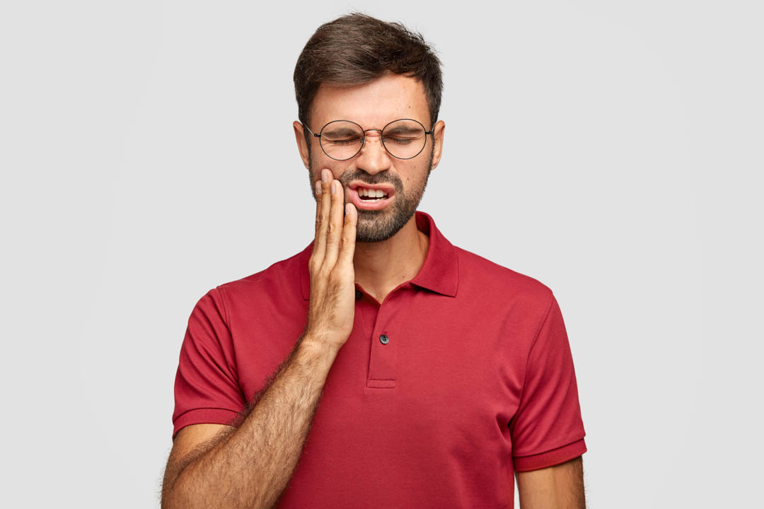 Hombre con dolor mandibular tocándose la cara con expresión de malestar, señal de posible bruxismo o TTM