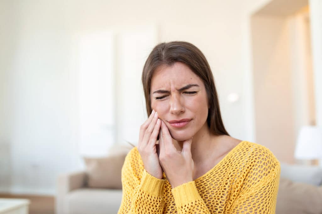 Mujer con dolor en la mandíbula debido al bruxismo, tocándose el rostro con expresión de malestar.